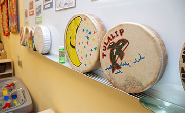 The Tulalip Betty J. Taylor Early Learning Academy official site - Culture and Language image of traditional hand drums in a classroom.